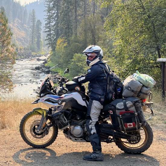 Peter Stace-Smith, on a fully-loaded adventure motorcycle beside a stream.